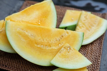 Pieces of ripe yellow watermelon on wicker table near swimming pool, closeup
