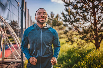Smiling man jogging in a park during sunrise with greenery and playground in the background