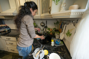 Woman tidying up the kitchen by doing the dishes in an atmosphere filled with domesticity and daily chores, at daylight in her own home