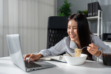 Asian young businesswoman eating noodles while working in the office.