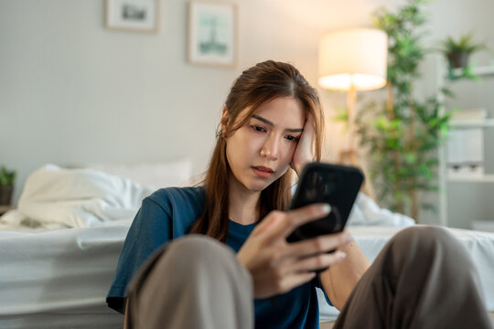 Asian young depressed woman looking at mobile phone in bedroom at home. 