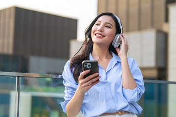 Asian woman enjoying music with headphones while standing in the city. 