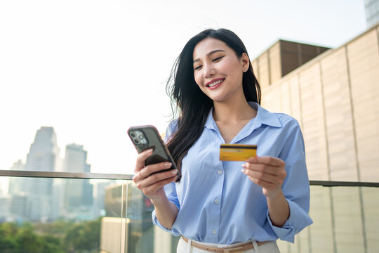 Asian woman using mobile phone shopping online outdoors in the city. 