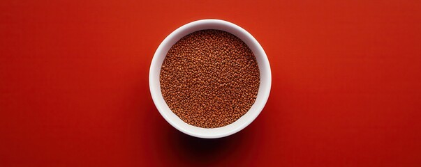 A white bowl filled with tiny mustard seeds sits centered on a vibrant red background.