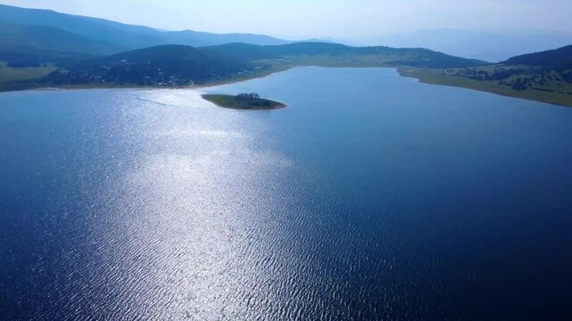 Aerial panoramic view of Batak Reservoir in Bulgaria captured by drone. Serene blue water, lush green forest and distant mountains create a peaceful, natural landscape from above.