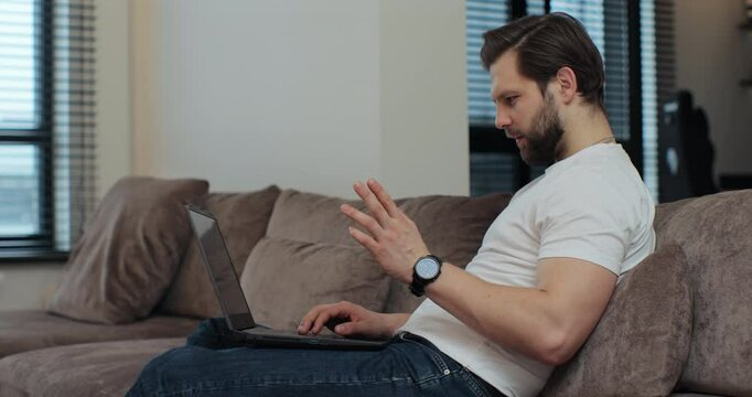 Young man resting on couch at home using laptop talk to family or friend on videoconferencing application. Virtual meeting working on laptop computer, video conference call.
