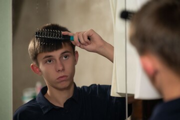 Young boy styling hair in front of a mirror in casual home setting during evening hours while...