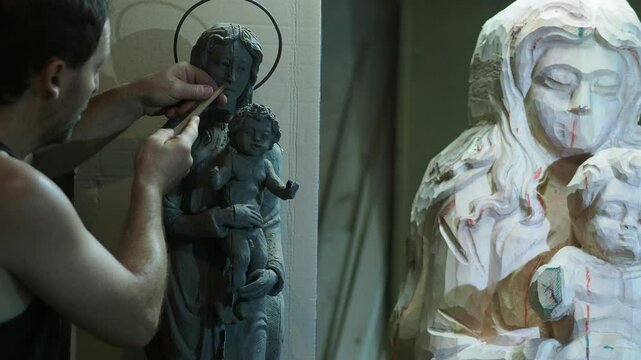 Professional sculptor carefully chiseling intricate details of wooden statue using traditional hand tools in controlled workshop environment, capturing precision of woodworking craft - real time