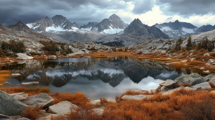 Mountain range reflecting in lake, with autumnal hues and cloudy skies