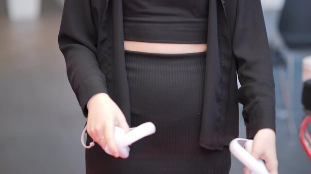 Woman in a black dress holding two white controllers. Concept of playfulness and fun, as the woman is likely engaging in a video game or interactive activity