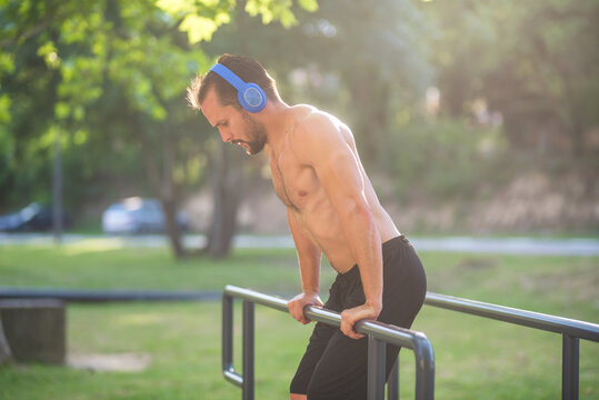 Young man wearing headphones doing dips on parallel bars in a park