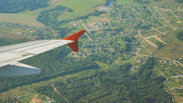 Airplane wing flying over green fields and a residential area