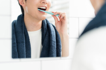 洗面所で鏡を見ながら歯を磨いている若い日本人男性