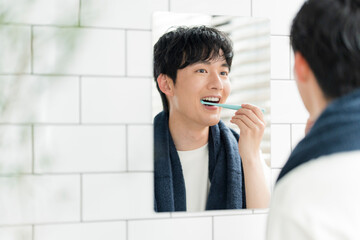洗面所で鏡を見ながら歯を磨いている若い日本人男性