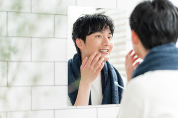 洗面所で鏡を見ながら歯を磨いている若い日本人男性