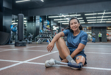 portrait of active asian female with prosthetic leg sitting on floor,resting during exercise in gym fitness club