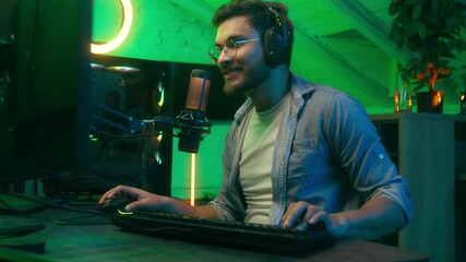 Emotional smiling man male happy talking in microphone video game win victory applause cheering winning addict Caucasian guy streamer gamer wearing headphones playing virtual battle computer at night