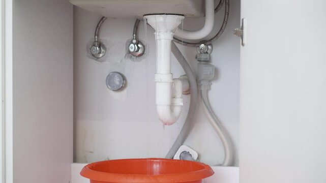 Detailed macro shot of water dripping into a container under a bathroom sink due to a faulty drain trap.
