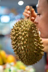 Cautious woman sniffing durian on grocery food counter. Rejection of exotic food, strong pungent aroma felt, Asian food inspection, tropical fruit smell, choosing food in shop grocery market