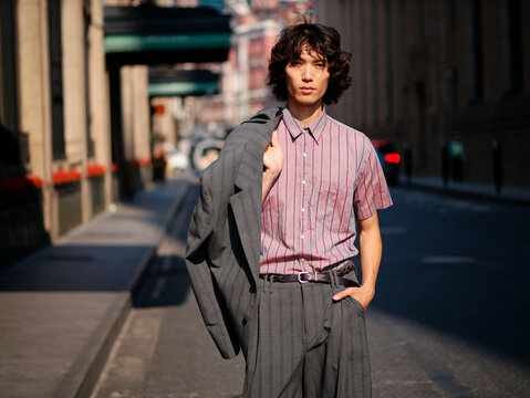 Portrait of handsome Chinese young man wearing stripe shirt posing in the street, young guy with black curly hair with urban background. Male fashion, cool Asian young man lifestyle. - Powered by Adobe