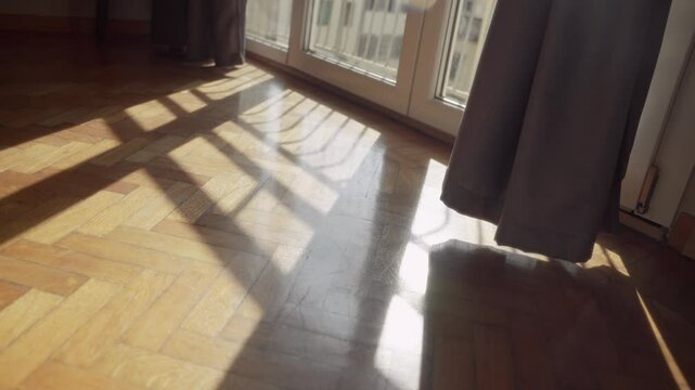 Shadows of sunlight entering from balcony window in apartment during daytime. Beautiful sun shining through as camera pulls away. Bedroom or hotel in early morning. Parquet floor inside European room