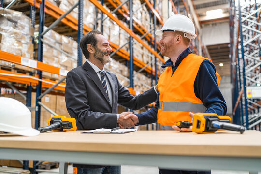 Manager and worker shaking hands in warehouse, logistics, delivery, distribution, supply chain, teamwork, partnership, success