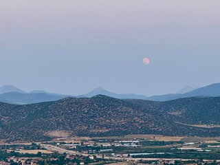 View of the Moon over mountains and a cozy city. Serene, dramatic, and magical night scene. Strawberry moon
