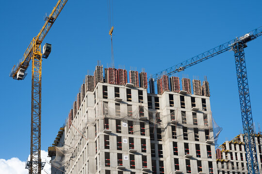 Tower cranes operating on a construction site, shaping a modern building against a clear blue sky, highlight urban development and engineering