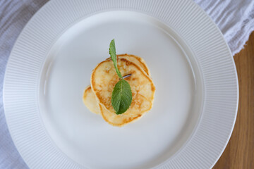 Small stack of pancakes garnished with fresh mint leaves on a white plate, simple breakfast concept