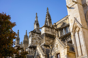 Fototapeta premium Close up of the exterior walls of Bordeaux Cathedral, featuring Gothic architectural details such as windows, pointed arches, pinnacles, and gargoyles under a blue sky. Bordeaux, Gironde, France.
