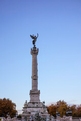 Fototapeta premium Monument aux Girondins on Place des Quinconces, featuring a tall column topped with the statue of Liberty and bronze sculptures at its base, surrounded by autumn trees. Bordeaux, Gironde, France.