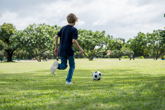 Little boy playing football in the garden with morning sunrise