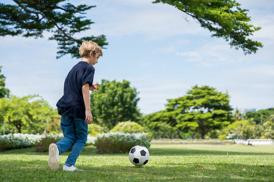 Little boy playing football in the garden with morning sunrise