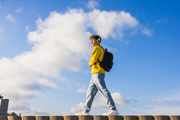 College student listening to music while walking on a wall under blue sky