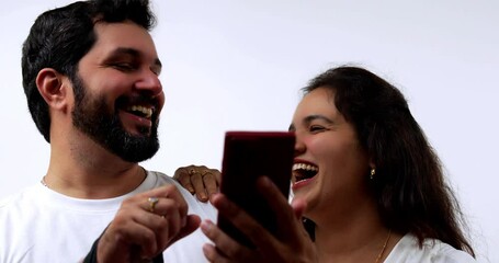 Indian couple with shopping bags isolated on white background, smiling and pointing at smartphone map or holding debit credit card with excitement, showing joyful expressions and retail enthusiasm
