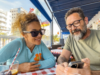 Happy middle-aged couple eating pizza together at a casual restaurant, taking selfies, checking...
