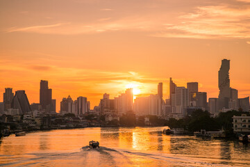 Sunrise over Chao Phraya River in Bangkok with city skyline, as water taxi cruises through golden reflections.
