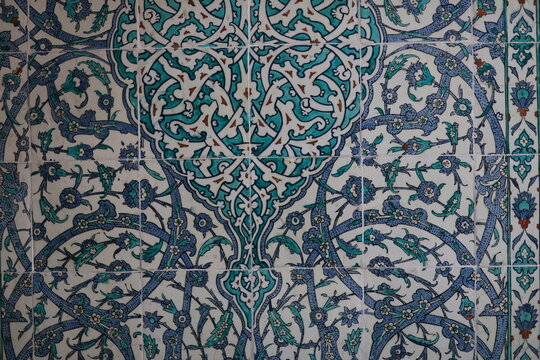 Elegant Islamic ceramic tiles with a symmetrical floral and arabesque design in turquoise, navy blue, and white, forming a stylized tree-like motif.