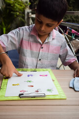 Smart Indian little boy perform thumb painting with different colourful water colour kit during the summer vacations, Cute Indian Kid doing colourful thumb painting drawing on wooden table