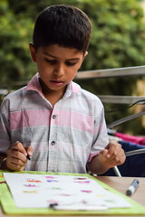 Smart Indian little boy perform thumb painting with different colourful water colour kit during the summer vacations, Cute Indian Kid doing colourful thumb painting drawing on wooden table