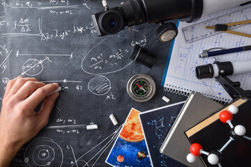 Student hand doing astronomical calculations on blackboard with educational material