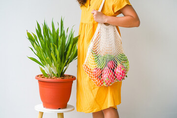 Woman holding mesh shopping bag with organic apple, corn, carrot, dragon fruit and lettuce on white background. Reusable shopping bag. Zero waste. Plastic free. Eco friendly concept.