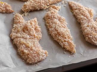 Close-up photo of raw chicken fillets coated with coconut shreds in a tray, ready to bake. Fresh, healthy, and flavorful tropical dish preparation.