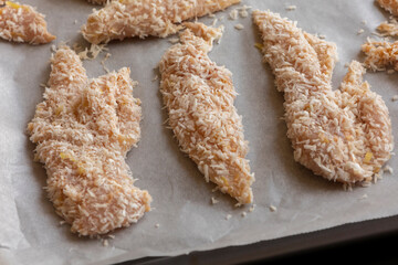 Close-up photo of raw chicken fillets coated with coconut shreds in a tray, ready to bake. Fresh, healthy, and flavorful tropical dish preparation.