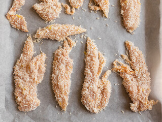 Close-up photo of raw chicken fillets coated with coconut shreds in a tray, ready to bake. Fresh, healthy, and flavorful tropical dish preparation.