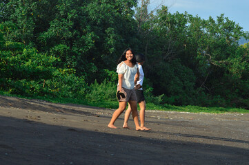With sandals in hand and smiles on their faces, the girls enjoy a slow stroll on black sand surrounded by tropical greenery and morning sunshine