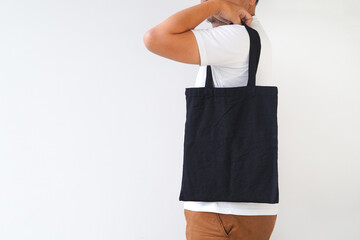 Young man hand holding black canvas tote bag on white background. Reusable eco bag for shopping. Eco friendly concept. Mockup for you designs.