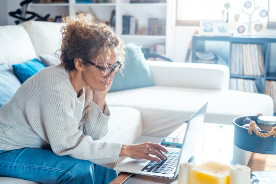 Fototapeta Middle-aged woman working from home on laptop. Mature female freelancer showing different facial expressions, from smiling to thoughtful. Concept of remote work, focus, creativity and modern digital l