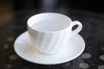 White cup of hot water with coaster on black table close up