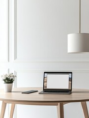 Minimalist workspace laptop with blank screen, phone, small potted plant on light wood table against white paneled wall, pendant lamp overhead